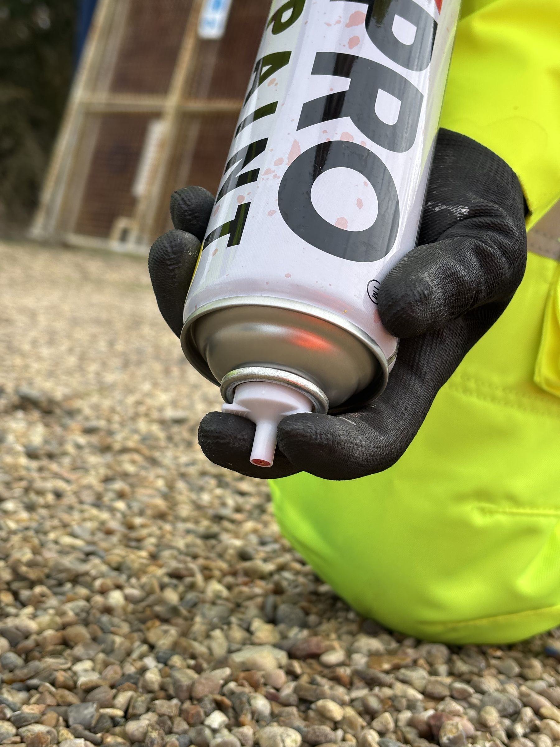 Close-up of a gloved hand holding a MarkPro can inverted, nozzle pointing down